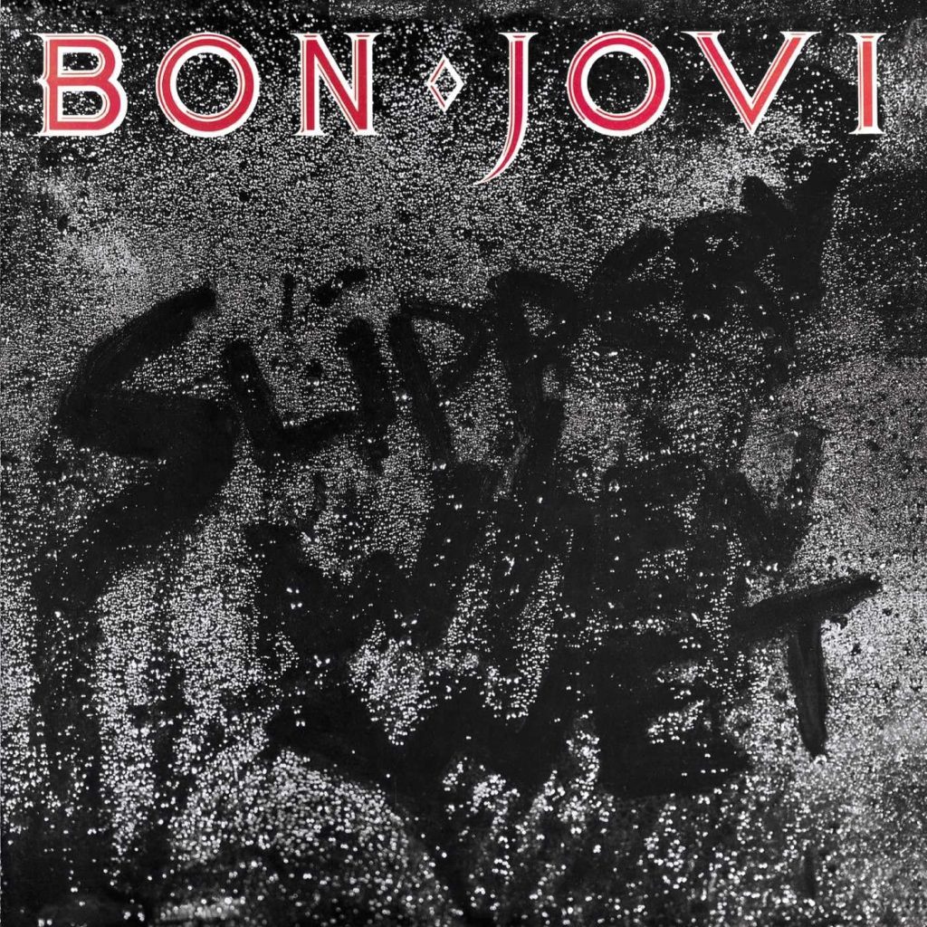 Cover art of Slippery When Wet by Bon Jovi featuring a black, rain-soaked surface with the band’s name in red at the top and the words Livin on a Prayer scrawled across the wet background.