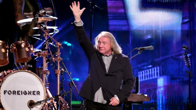 Classic rock artist performs live under dramatic stage lighting with guitar in hand.