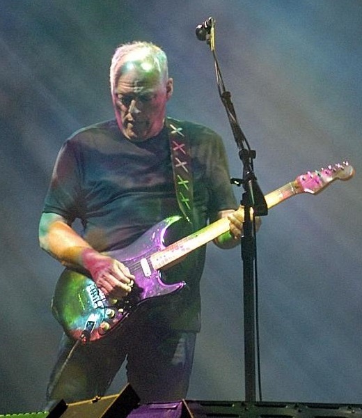 David Gilmour Live in Concert - Classic Rock Artists David Gilmour performing live on stage with his iconic Stratocaster guitar under colorful stage lighting.