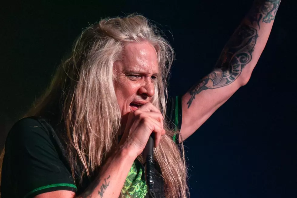 Sebastian Bach Dynamic Stage Performance - Classic Rock Artists Rock vocalist Sebastian Bach with long hair and tattoos raising their arm while singing into a microphone.