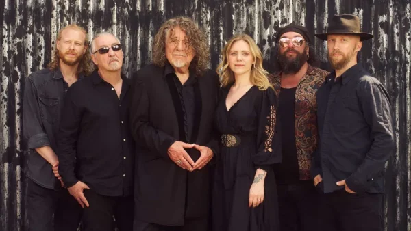 Robert Plant and Saving Grace - Gospel Plough Recording Artists Photo - Classic Rock Artists Robert Plant and Saving Grace band members pose together in black clothing against weathered wooden backdrop, the creative team behind Gospel Plough single.