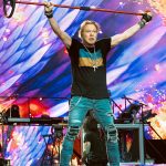 Guns N' Roses members: Axl Rose performing live on stage holding a microphone stand above his head during a concert in London 2022.