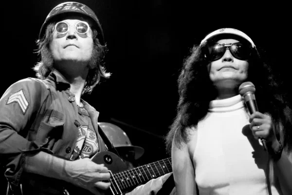 John Lennon Live Performance 1972 Madison Square Garden - Classic Rock Artists John Lennon live performance with Yoko Ono on stage in 1972, both wearing sunglasses and military-style clothing.