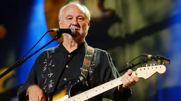 Sonny Curtis Live Performance - Classic Rock Legend with Fender Stratocaster - Classic Rock Artists Sonny Curtis performing on stage with his white Fender Stratocaster guitar and microphone, wearing a black shirt with decorative embroidery against a blue-lit concert backdrop.