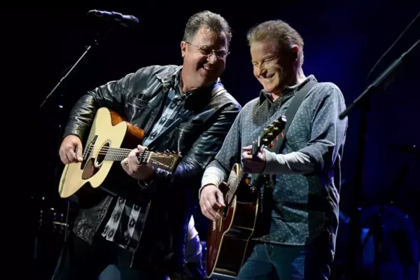 Eagles Members Don Henley and Joe Walsh Perform Live on Stage - Classic Rock Artists Don Henley and Joe Walsh performing together on stage during The Eagles tour, both holding acoustic guitars and smiling under stage lighting.
