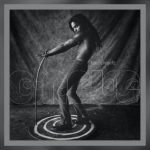 Alt Text: Lenny Kravitz Circus Deluxe 30th anniversary album cover featuring black and white artistic photo of shirtless performer with long hair in dynamic pose surrounded by circular ripples on textured ground.