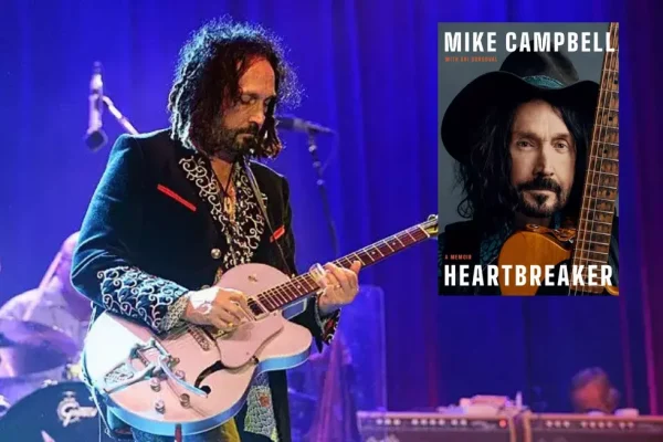 Alt Text: Mike Campbell and the Dirty Knobs guitarist performing live on stage with his signature white Telecaster guitar under blue stage lighting, with his memoir "Heartbreaker" book cover visible in the corner.