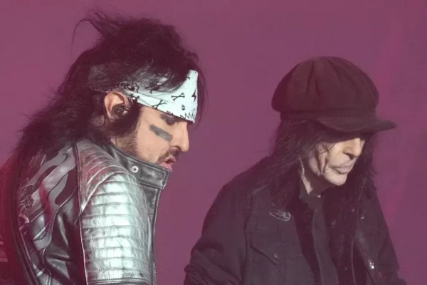 Mick Mars and Motley Crue Bandmate Live Performance - Classic Rock Artists Alt Text: Mick Mars Motley Crue guitarist performing on stage in silver leather jacket and white bandana alongside bandmate in black clothing during live concert.