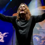 Ozzy Osbourne tribute performer on stage with arms raised during live rock concert with dramatic blue and orange lighting.