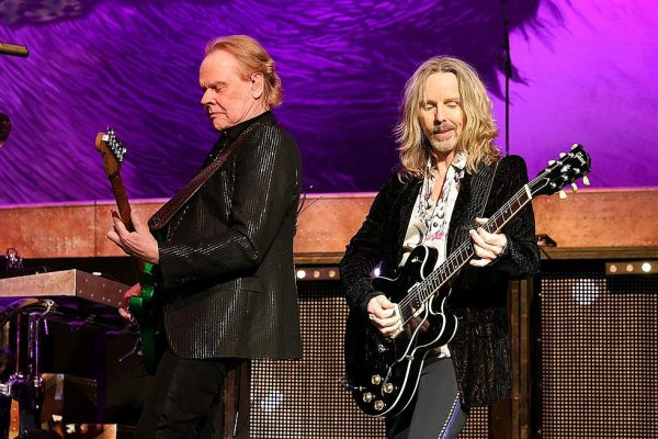 Styx Concert Live Performance - Tommy Shaw and James Young on Stage - Classic Rock Artists Two Styx guitarists performing live on stage during a Styx concert, with purple stage lighting and one guitarist wearing a sparkly black jacket while the other plays a black Gibson guitar.