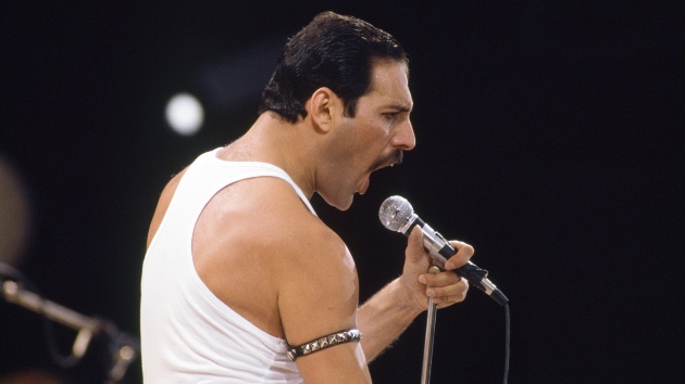 Freddie Mercury performing live in white tank top holding microphone, featured in A Life in Lyrics book announcement.