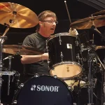 Phil Rudd Playing Drums Live Performance - Classic Rock Artists Phil Rudd AC/DC drummer performing behind black Sonor drum kit with Sabian cymbals.