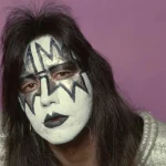 Ace Frehley Dead at 74 - The Spaceman in His Iconic Kiss Makeup - Classic Rock Artists Ace Frehley in iconic Spaceman makeup featuring silver star design over his eyes and black lightning bolts on white face paint, wearing a silver sequined costume against a purple background.