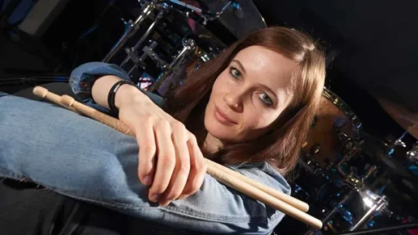 Anika Nilles the drummer holding drumsticks and smiling at camera from behind drum kit.