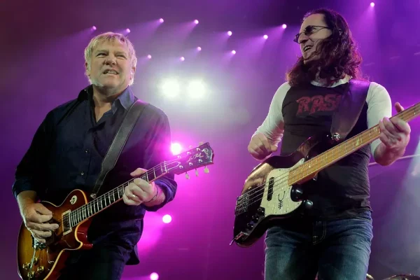 Geddy Lee and Alex Lifeson performing on stage during Rush Fifty Something Tour announcement with purple lighting ``` **Title:** ``` Rush Fifty Something Tour - Geddy Lee and Alex Lifeson Live Performance ``` **Description:** ``` Rush legends Geddy Lee (bass) and Alex Lifeson (guitar) performing together on stage under dramatic purple lighting. The iconic duo announced their Rush Fifty Something Tour 2026 reunion, marking their first performances in over a decade and honoring the legacy of late drummer Neil Peart.