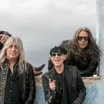 Scorpions From The First Sting - German Rock Legends Celebrate 60 Years - Classic Rock Artists Scorpions From The First Sting 60th anniversary band photo featuring Klaus Meine, Rudolf Schenker, Matthias Jabs, Pawel Maciwoda and Mikkey Dee against graffiti wall.