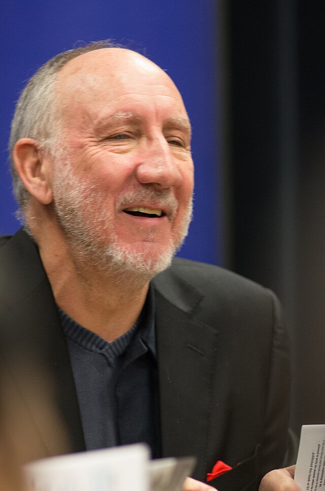 The Who Pete Townshend smiling during a public appearance, wearing a black blazer over a dark shirt
