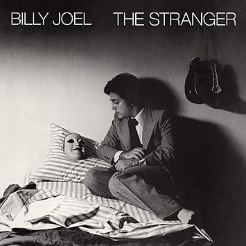 The Stranger Billy Joel 1977 album cover featuring man in suit lying on bed with boxing gloves and mask