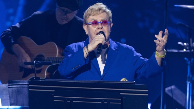 Elton John teases two new albums while performing at piano in signature blue suit and sunglasses