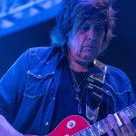 Dean DeLeo performing live on stage with a red electric guitar, showcasing his signature playing style and tone as Stone Temple Pilots’ guitarist.
