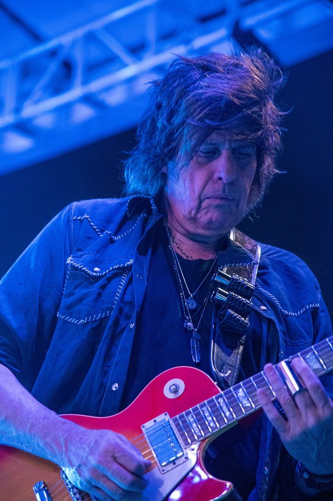 Dean DeLeo performing live on stage with a red electric guitar, showcasing his signature playing style and tone as Stone Temple Pilots’ guitarist.