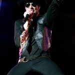 Scott Weiland performing live in leather jacket and fedora hat with microphone.