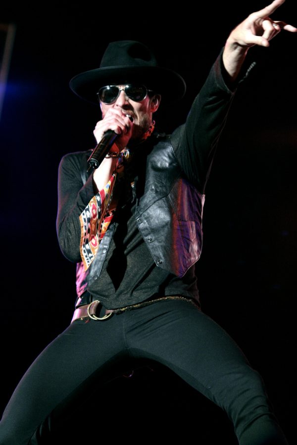 Scott Weiland performing live in leather jacket and fedora hat with microphone.