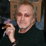 A portrait of Dewey Martin, the legendary Buffalo Springfield drummer, wearing tinted glasses and holding a cigar.