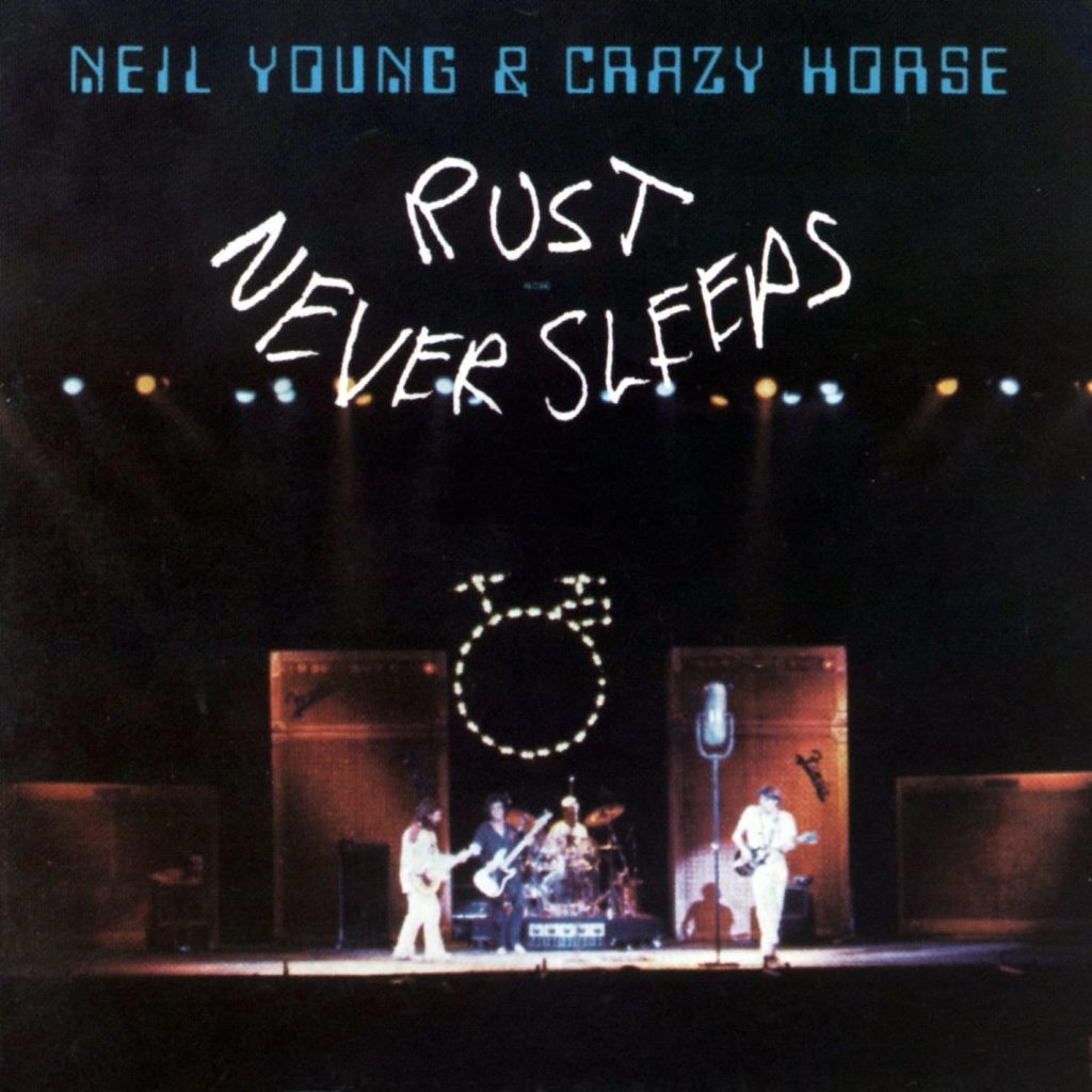 Rust Never Sleeps album cover showing Neil Young and Crazy Horse performing on stage with oversized microphones and hand-drawn title text