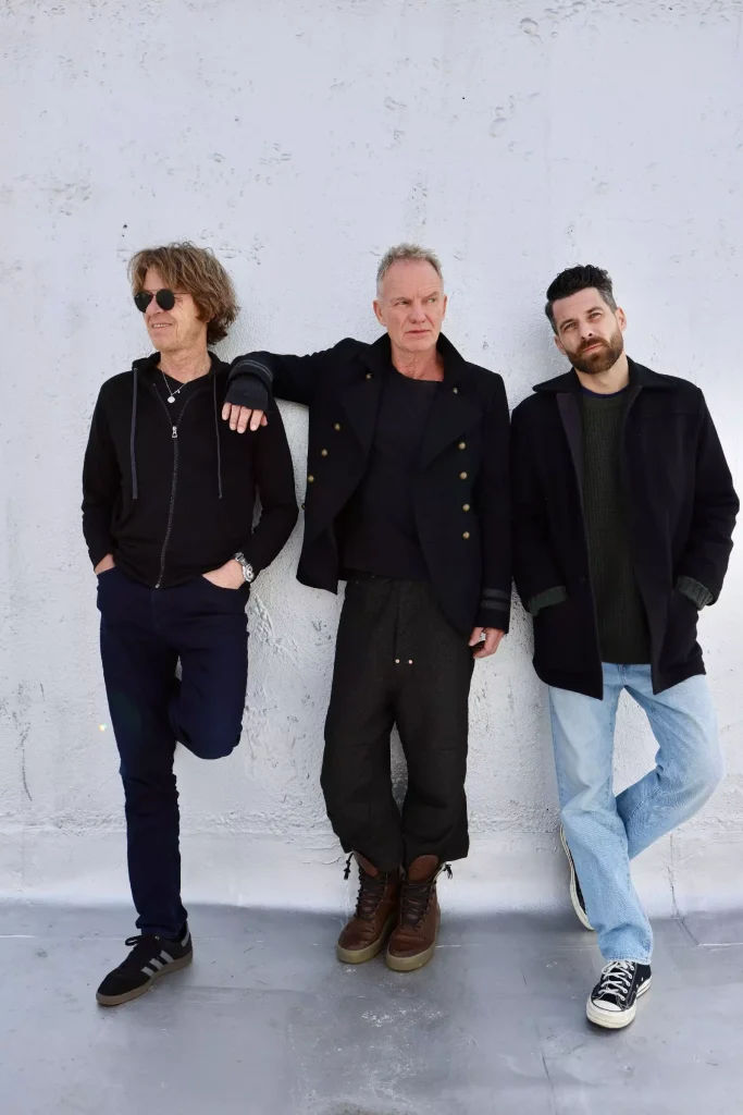 Sting, Dominic Miller, and Chris Maas leaning against a white wall for a sting tour promotional photo.