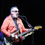 Elvis Costello performing live with his signature horn-rimmed glasses and guitar