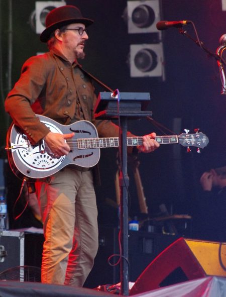 Les Claypool performing live with his custom bass, the defining image of a four-decade career