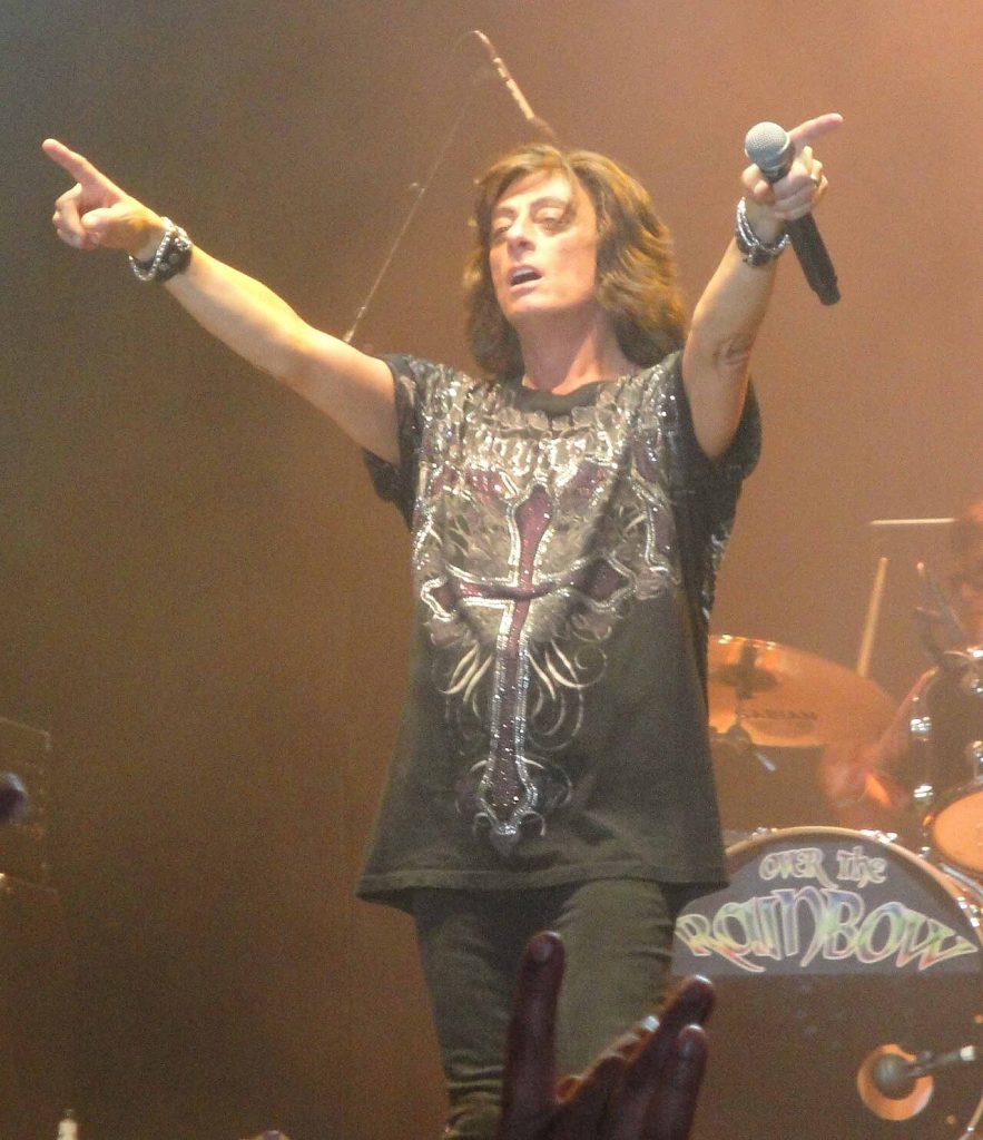 Joe Lynn Turner performing live on stage during a Rainbow concert, holding a microphone and pointing to the crowd.